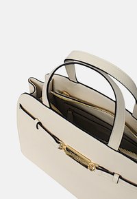 Borsa a mano in pelle beige con dettagli neri, texture liscia e hardware dorato. Presenta manici doppi e un compartimento interno con zip.