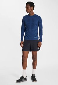 Marinblå långärmad tröja med en logga i mitten, kombinerad med svarta shorts. Outfitten har en sportig design och material för träningskläder.