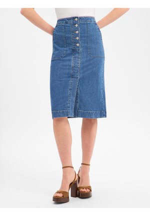 Jupe midi en denim avec des boutons devant, deux grandes poches à l'avant et une fente frontale, portée avec des talons compensés marron.