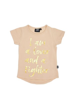 T-shirt à manches courtes couleur pêche, avec une inscription dorée : « Je suis une personne aimante et une battante. »