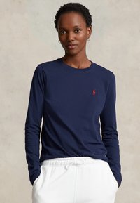 Tamsiai mėlynos ilgomis rankovėmis t-shirt'as, pagamintas iš medvilnės, su maža raudona polo logotipu kairėje krūtinės pusėje. Dėvimi su baltais sportiniais džinsais su raišteliais.