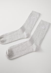 Chaussettes rayées gris clair avec une texture lisse, arborant un logo circulaire blanc sur la bande supérieure. La longueur atteint le milieu du mollet.