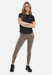 Črna kratka majica s kratkimi rokavi in logotipom, olivno zeleni legingi z logotipom in črna športna obuvala; gladek material, prilegajoč dizajn.