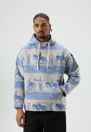 Capuchontrui met een beige basis, blauw paarden- en cactuspatroon, een voorzak en een sluiting met trekkoord. Knusse textuur.