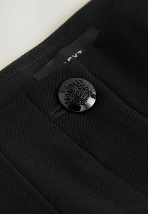 Tejido negro con una textura suave, que presenta un botón negro brillante adornado con un diseño detallado, parte de una prenda de vestir.