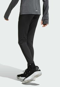 Crne atletske tajice s elegantnim dizajnom, izrađene od rastezljivog materijala, uparene s crno-bijelim tenisicama za trčanje s teksturiranim detaljima.