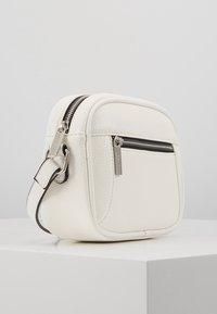 Borsa a tracolla bianca in pelle con finitura testurizzata, dotata di una tasca frontale con zip, accessori in argento e una tracolla regolabile.