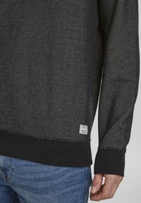 Sweatshirt noir à motif avec une surface texturée, doté d'un ourlet et de poignets côtelés. Comprend une petite étiquette au bord inférieur.