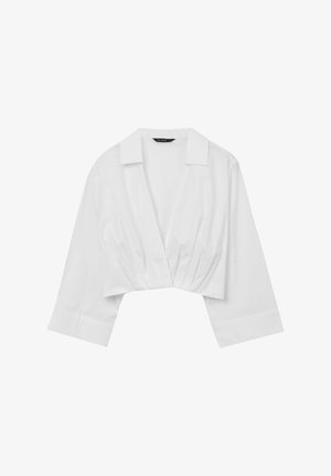 Blusa bianca corta con colletto, maniche 3/4 e dettagli plissettati sul davanti. Realizzata in tessuto leggero, con una texture liscia.