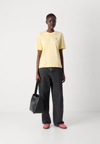 Gul bomull t-shirt med korta ärmar, kombinerad med svarta vida denimjeans. En svart handväska och rosa skor fulländar outfiten.
