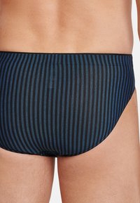 Simshorts i marinblått med vertikala ljusblå ränder. Tillverkade av smidigt tyg, med en tajt passform och elastisk midja.
