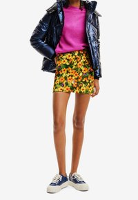 Kiiltävä tummansininen toppatakki, vaaleanpunainen neulepaita, kukallinen minihame keltaisilla ja oransseilla kukilla sekä siniset tennarit valkoisilla pohjilla.