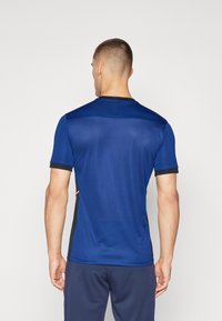 Blå treningsskjorte med korte ermer, svarte detaljer på ermene og sidene, glatt tekstur, rund hals, og pustende stoffdesign.