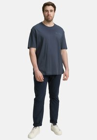 Marineblauwe katoenen T-shirt met korte mouwen, relaxte pasvorm en subtiel merkkapel. Geselecteerd met donkere broeken en witte sneakers.