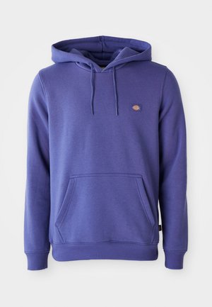 Lilla kapuutsiga sviiter, mis on valmistatud pehmest kangast. Sellel on känguru tasku, nöörid krae juures ja väike logo vasakul ülal.