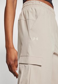 Pantaloni cargo beige realizzati in tessuto morbido, dotati di una vita elasticizzata, tasche laterali e un logo del brand discreto sulla coscia.