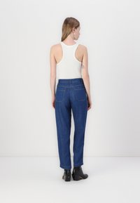 Jeans de ganga azuis de cintura alta com um corte relaxado, apresentando dois bolsos traseiros e costura visível, combinados com uma t-shirt justa branca.