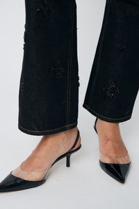Črne jeans hlače z cvetličnimi sequined detajli in rumenim šivom, v kombinaciji s črnimi patentnimi slingback petkami.