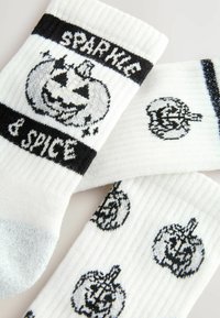 Weiße Socken mit schwarzen Kürbismotiven und dem Text "SPARKLE & SPICE." Rippstruktur; die Muster umfassen einen großen Jack-o'-Lantern und kleinere Kürbisse.