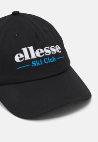 Svart caps med brodert hvit "ellesse"-logo og "Ski Club" i blått. Flat skygge og teksturert stoffdesign, seks ventilasjonshull.