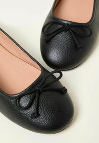 Schwarze Ballettflats aus Leder mit weicher Textur, runder Spitze und dekorativem Schleifen. Das Innere ist mit einem glatten, hellen Futter ausgestattet.