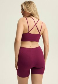 Fioletowy stanik z ribbowanego materiału z regulowanymi ramiączkami typu spaghetti oraz pasującymi ribbowanymi szortami. Posiada krzyżujące się plecy i miękką, elastyczną teksturę.