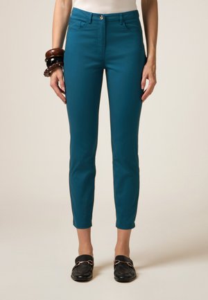 Pantaloni in misto cotone color turchese con vestibilità slim, tasche frontali e chiusura a bottone. In abbinamento a mocassini neri e bracciali in legno.