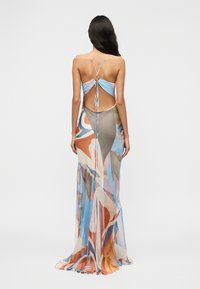 Μακρύ, πολύχρωμο διάφανο φόρεμα από ελαφρύ ύφασμα, με χαμηλή πλάτη, λεπτές τιράντες και αφηρημένα σχέδια σε μπλε, πορτοκαλί και ροζ.