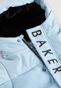 Ljusblå dunstjacka med svart fleecefoder, med en framträdande "BAKER"-etikett, tryckknappsstängning och slät textur.