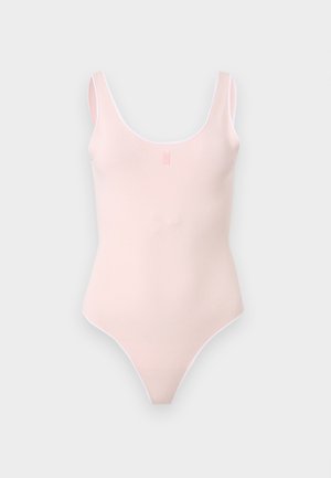 Γυναίκα στέκεται με το ένα χέρι στην τσέπη, φοράει λευκό αμάνικο μπλουζάκι, τζιν σορτς μήκους μέχρι το γόνατο με λουλουδένια κοψίματα, λευκές κάλτσες και μαύρα παπούτσια.