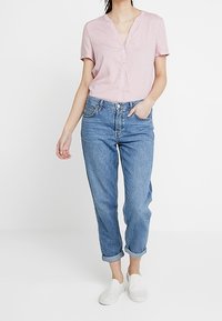 Chemise rose clair à manches courtes et col cranté, assortie à un jean droit à revers bleu et à des chaussures blanches à enfiler.