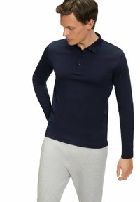Marineblaues Langarm-Polohemd mit Kragen und Drei-Knopf-Leiste, aus glattem Stoff, kombiniert mit hellgrauen Hosen.