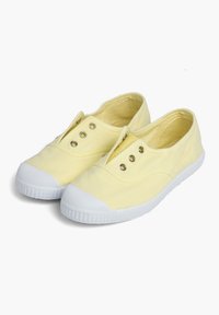 Żółte płócienne buty wsuwane z białymi gumowymi podeszwami i czubkami, posiadające mosiężne oczka i gładką teksturę.