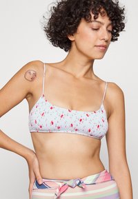 Bralette de padrão floral em azul claro com alças finas, tecido pregueado e textura franzida. Acentuado com pequenas flores vermelhas.