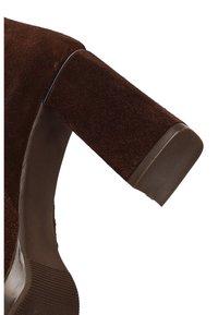 Zapato de tacón alto de ante marrón con superficie texturizada, con un tacón cuadrado y una suela de goma oscura y lisa.