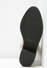 Sole di scarpa beige con fondo in gomma nera testurizzata, caratterizzata da una forma arrotondata. Le marcature includono "HECHO EN ESPAÑA" e la taglia "37."