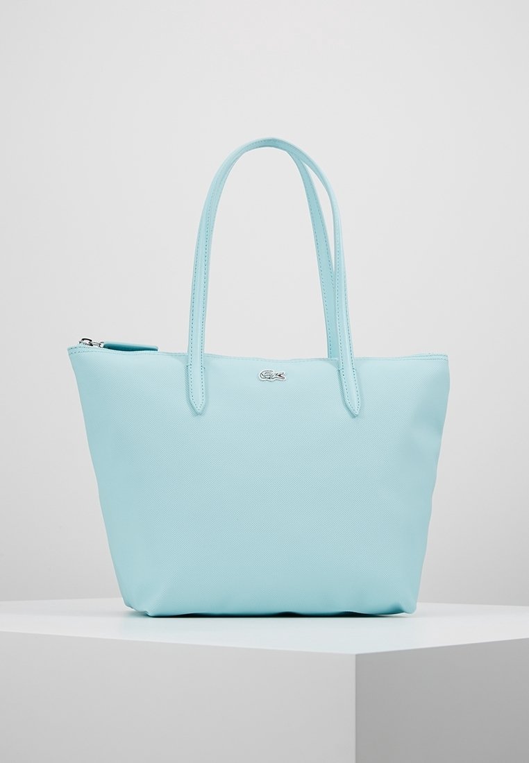 Sac tote bleu clair en matériau synthétique texturé. Dispose de deux poignées et d'une fermeture éclair avec un petit accent logo en argent.
