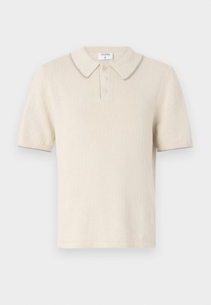 Krämfärgad polo-shirt med korta ärmar, ribbad textur, treknappars placket och en kontrasterande krage. Materialet ser mjukt och lätt ut.