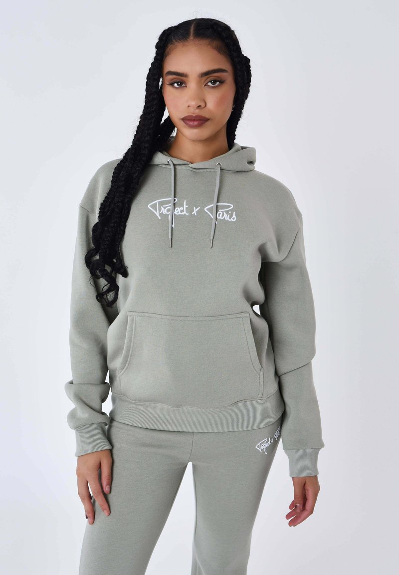 Lichtgroene hoodie en bijpassende broek van zacht materiaal, met een voorste kangoeroezak en een wit geborduurd logo op de borst.