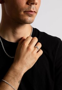 Sølv ring med flere sten båret på hånden, parret med en sølv kæde halskæde. Personen har en sort skjorte på.