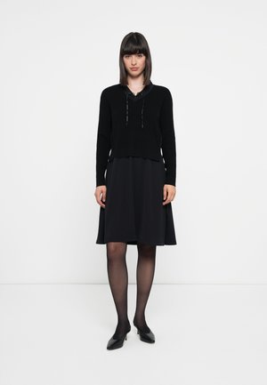 Zwarte sweater met capuchon ontwerp, gecombineerd met een vloeiende zwarte jurk; beide stukken hebben een zachte textuur en een getailleerd silhouet.