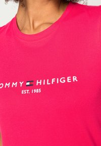 T-shirt rosa brillante, realizzata in morbido cotone, con scollatura rotonda e il logo ricamato "TOMMY HILFIGER EST. 1985" in bianco.