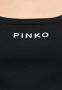 Κοντινό πλάνο από μαύρο ριμπ ύφασμα σε μπλούζα με λευκό λογότυπο "PINKO" σε κεφαλαία γράμματα, τοποθετημένο στο κέντρο κοντά στη γραμμή του λαιμού.