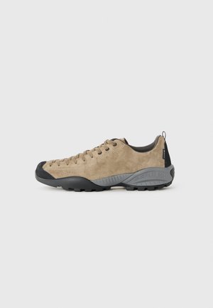 Brune semskede fottursko med svart gummisåle, tåhette og oppheving, med snøring og Scarpa-merke på siden og hælen.