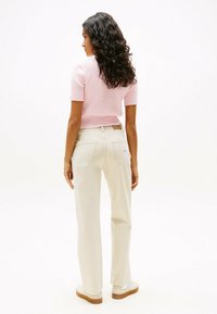 Korte roze geribbelde gebreide top met korte mouwen, gecombineerd met licht beige rechte broek. Witte sneakers met een bruine zool en labeldetails.