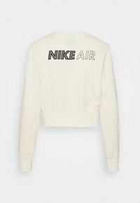 Sweatshirt cropped crème avec le texte noir "NIKE AIR" au dos, des poignets côtelés et un col rond. Texture de tissu lisse.