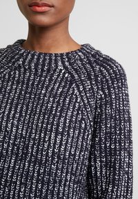 Mörkblå och vit randig stickad tröja med en strukturerad mönster, rundad halsringning och raglanärmar. Mjukt material med synligt garn.