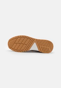 Suela de zapato con una suela exterior de goma texturizada, que presenta patrones angulares y una sección de entresuela blanca para mayor agarre y durabilidad.