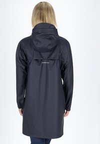 Granatowa, wodoodporna kurtka przeciwdeszczowa z kapturem, elastycznymi mankietami i wysokim wentylowanym tyłem. Posiada logo na górnej części pleców. Długość sięga do połowy uda.