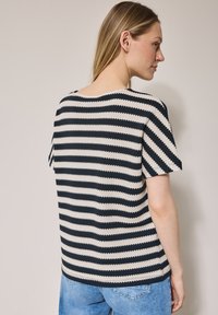 Randig stickad T-shirt med horisontella marinblå och krämfärgade ränder, korta ärmar och en avslappnad passform. Texturerat mönster genom hela plagget.